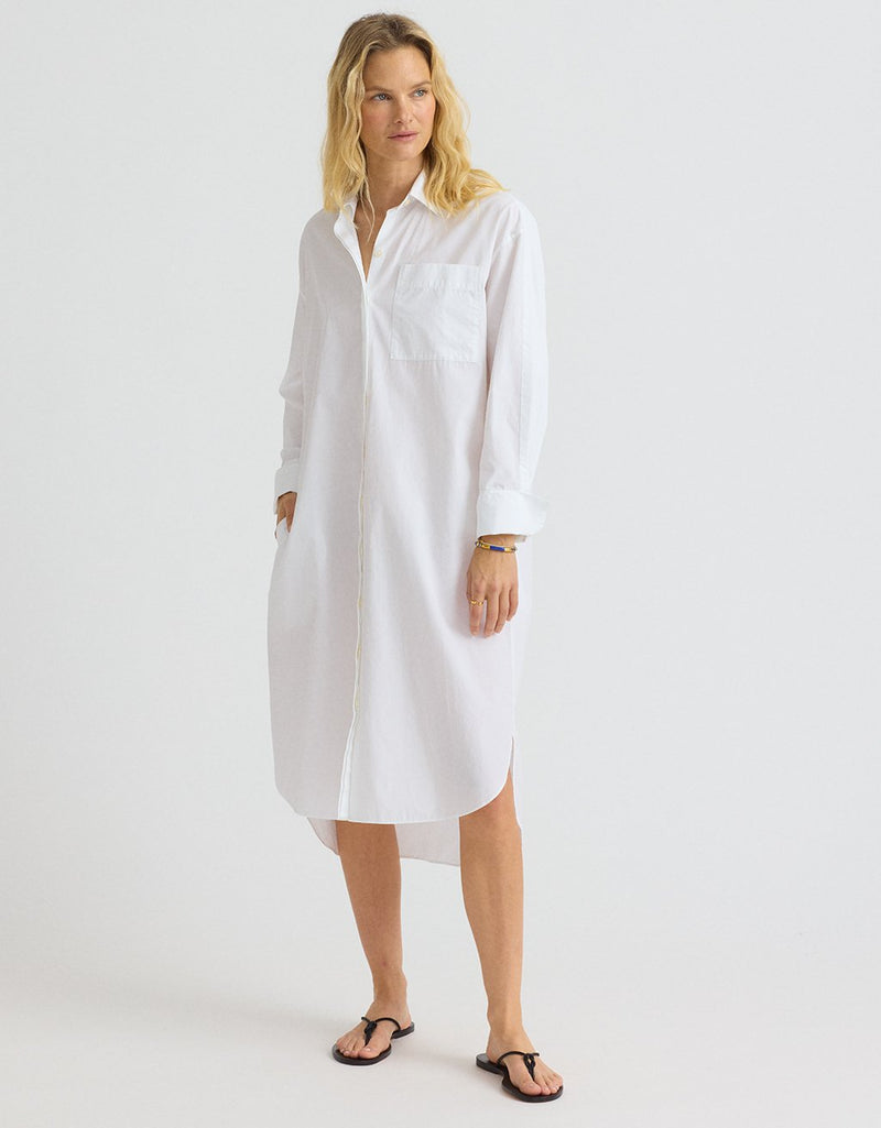 Woman wearing a white shirtdress and black sandals on a plain background