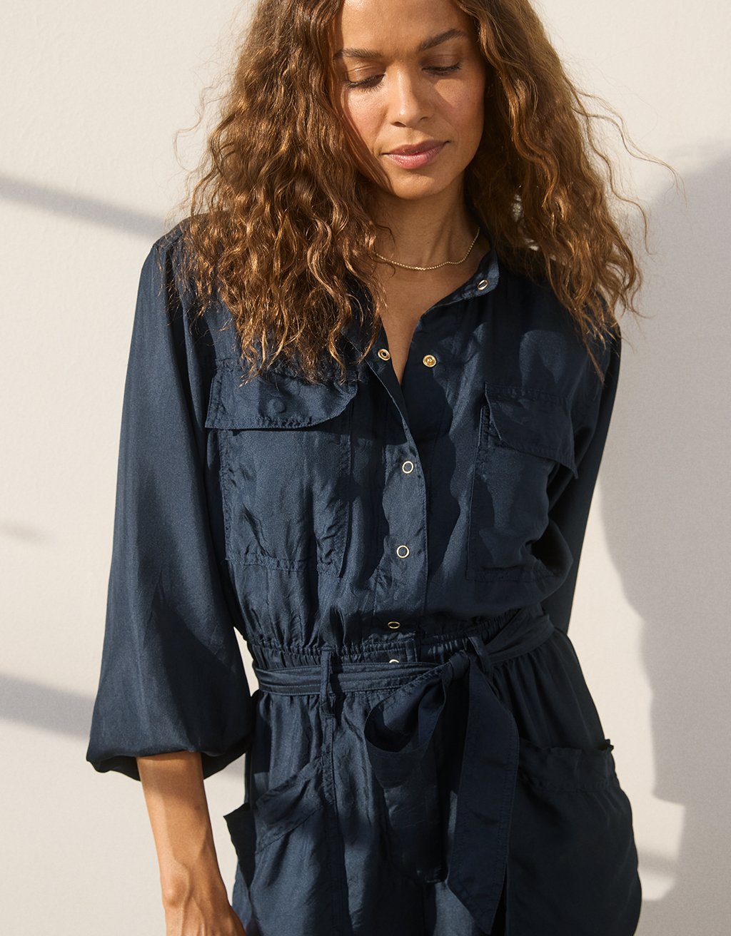 Close-up of a woman wearing a navy blue utility silk jumpsuit against a light background