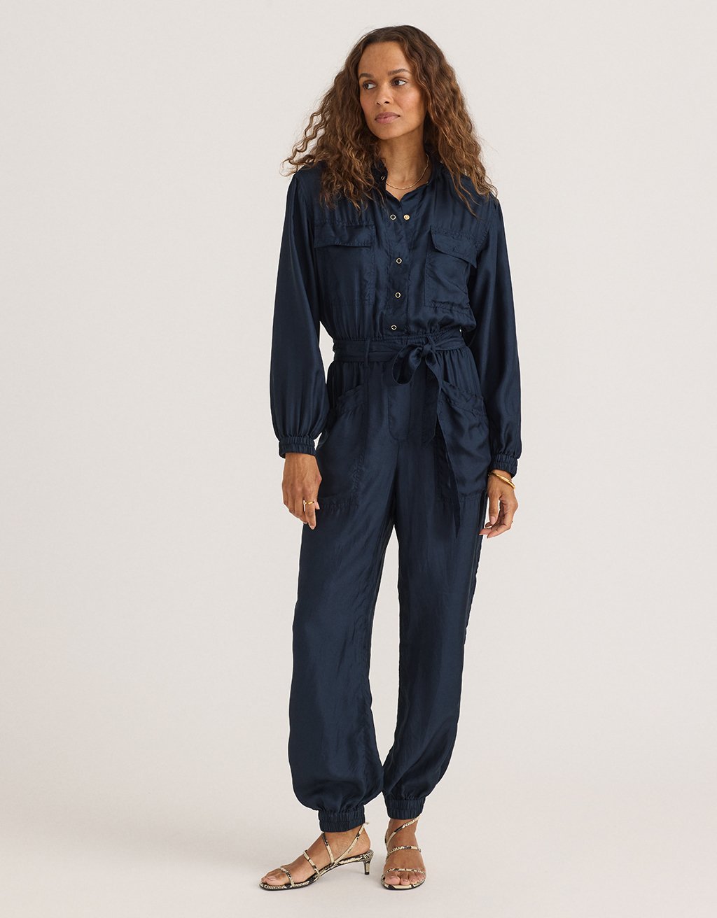 Woman wearing a navy blue silk utility jumpsuit on a light gray background
