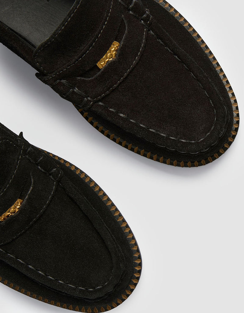 Close-up of black suede loafers with gold accents and contrast stitching details on a white background