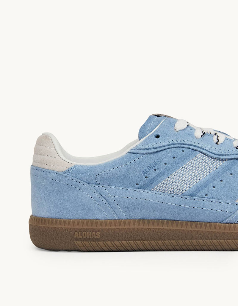 Close-up of a cornflower blue sneaker with white accents and a rubber sole on a light gray background