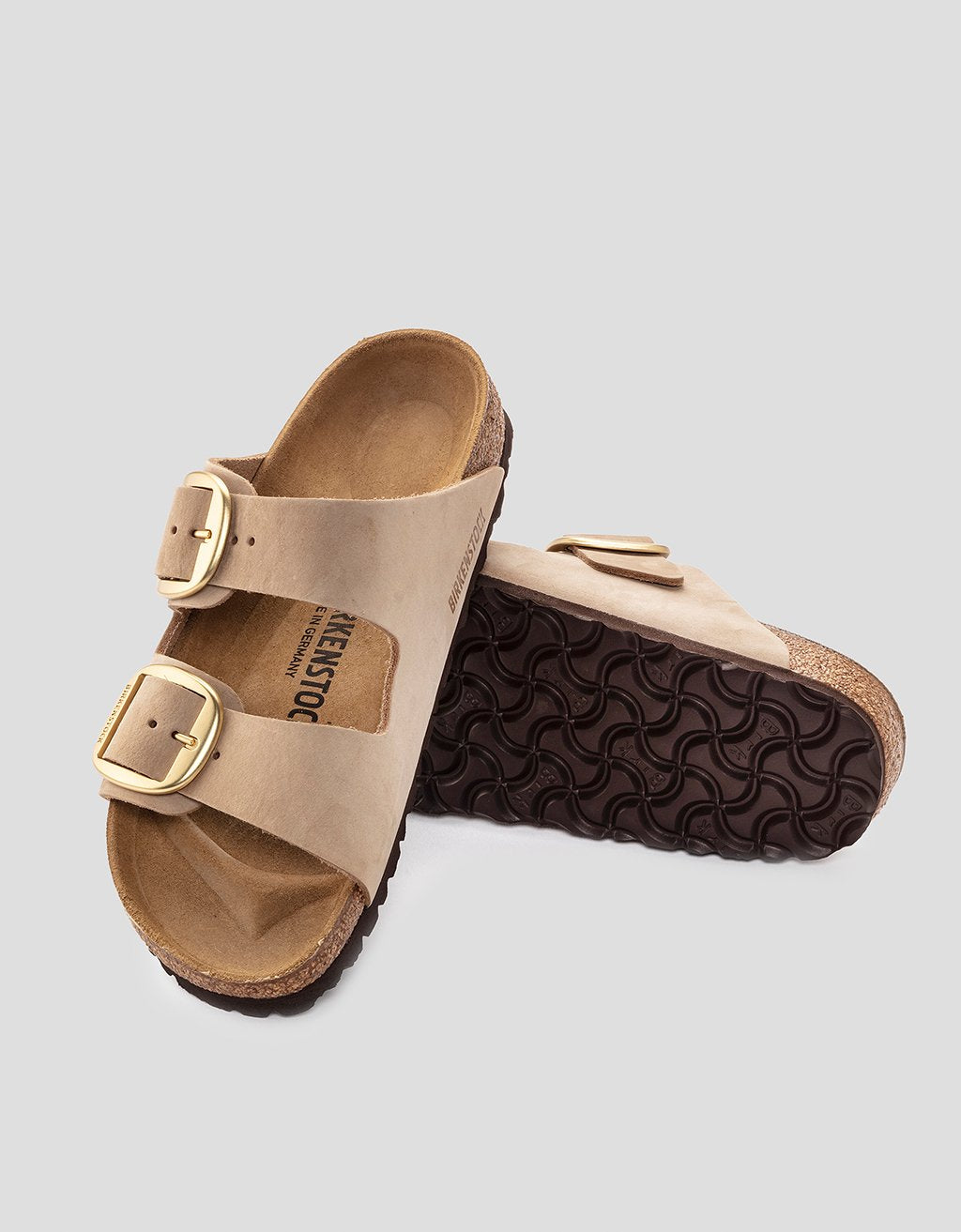 Pair of tan Birkenstock sandals with gold buckles on a light gray background