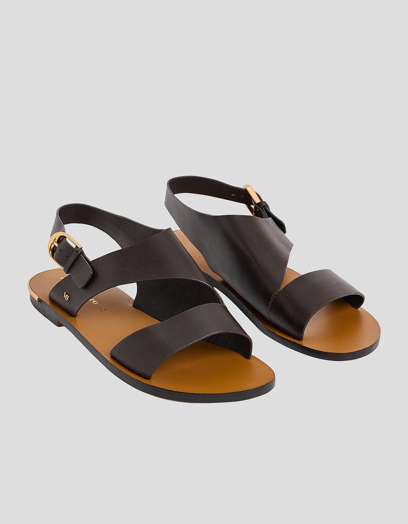Side view of a brown leather sandal with a gold buckle ankle strap on a light gray background