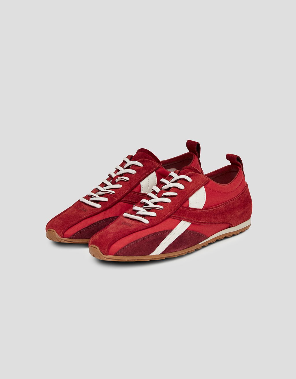 Red leather sneakers with white laces and rubber soles on a light gray background