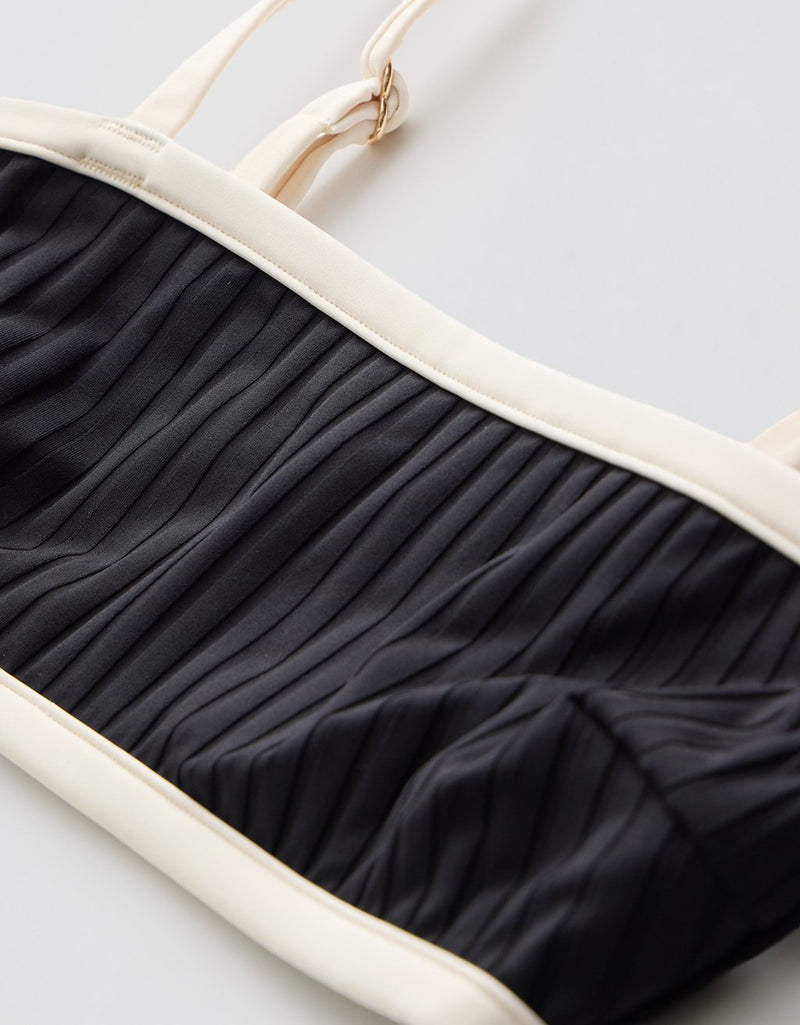 Black ribbed bikini top with contrast ivory straps and trim on a light gray background